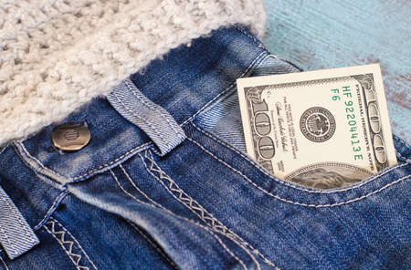 100 Dollars in jeans pocket on blue wooden background