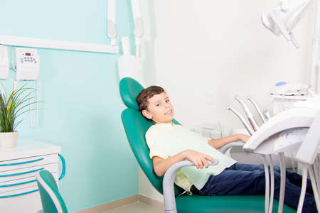 Little cute kid smiling while sitting in chair at dental clinicの写真素材