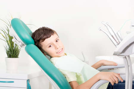 Little cute kid smiling while sitting in chair at dental clinicの写真素材