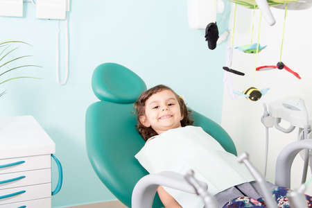 Little cute girl smiling while sitting in chair at dental clinicの写真素材