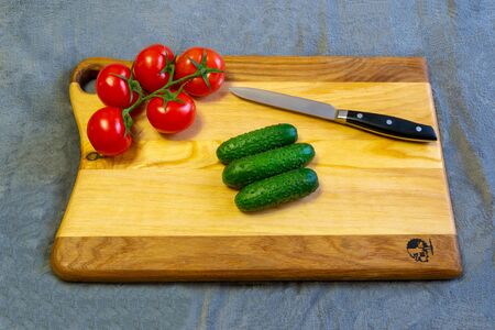 Cucumbers, tomatoes and knife on a beautiful chopping boardの写真素材