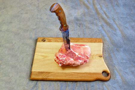 The knife thrust in a piece of meat on a beautiful chopping boardの写真素材