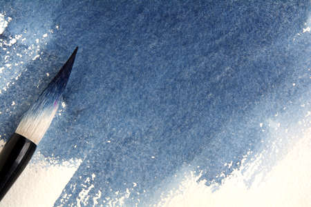 Calligraphic brush stained with blue paint on a sheet of watercolor paper with indigo stain.の写真素材