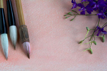 Chinese watercolor brushes on a pink-tinged watercolor sheet adorned with purple wildflowers.の写真素材