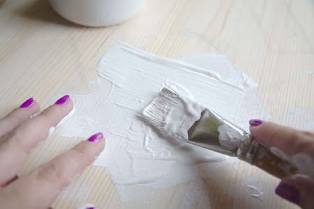 Priming of a wooden panel for painting with white acrylic primer using a bristle brush. Hands in the frame.の写真素材