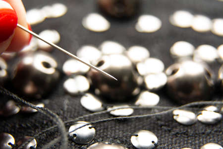 Silver shiny beads and sequins in vintage style are sewn on black coarse fabric. In the frame, a needle with thread.の写真素材