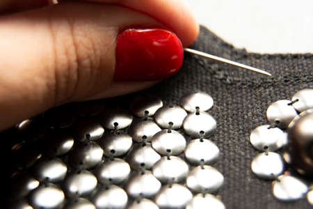 Silver shiny beads and sequins in vintage style are sewn on black coarse fabric. In the frame of the hand. In the frame, a needle with thread.の写真素材