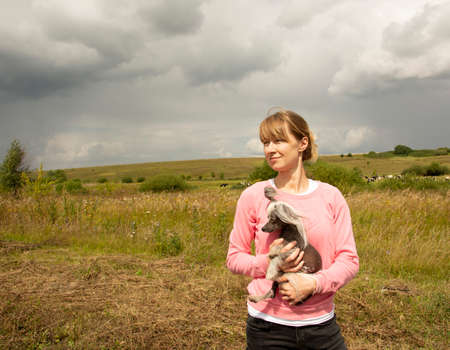 A middle-aged woman squints at the sun. A middle-aged woman in a pink sweatshirt enjoys a walk in nature and holds a small dog in her arms.の写真素材