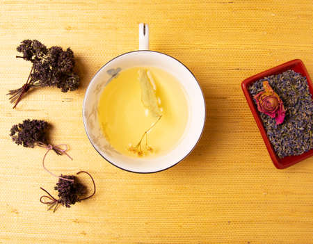 Cup of herbal tea in a porcelain cup with various herbs on yellow background. Linden tea, tea with rose buds, tea with lavender, tea with oregano.の写真素材