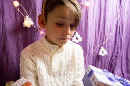 A 10-year-old European boy receives Christmas gifts, his face expresses doubt.の写真素材