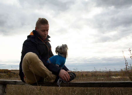 A middle-aged man walks with a dog breed Chinese Hairless Crested Dog on nature in autumn afternoon.