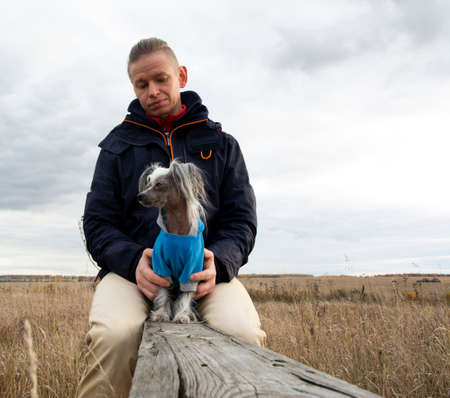 A middle-aged man walks with a dog breed Chinese Hairless Crested Dog on nature in autumn afternoon.の写真素材