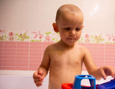 Happy little boy in the bathroom playing with plastic toy boat. Infant training and bathing. Hygiene...