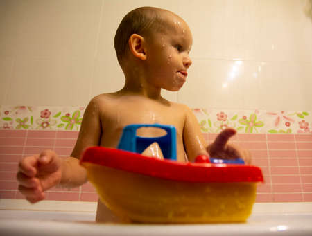 Happy little boy in the bathroom playing with plastic toy boat. Infant training and bathing. Hygiene and care for young children.の写真素材