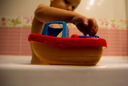 Happy little boy in the bathroom playing with plastic toy boat. Infant training and bathing. Hygiene...