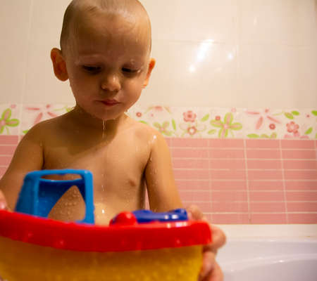 Happy little boy in the bathroom playing with plastic toy boat. Infant training and bathing. Hygiene and care for young children.の写真素材