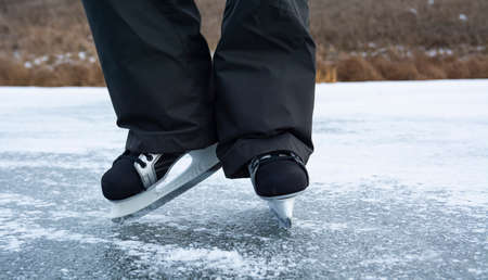 Legs of a man in men's skates on the ice of a wild river. Winter outdoor recreation in the countryside.の写真素材