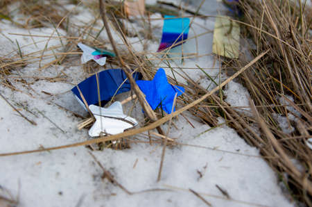 Confetti lie in the snow after the holiday. Natural meadow covered with garbage. Ecological...