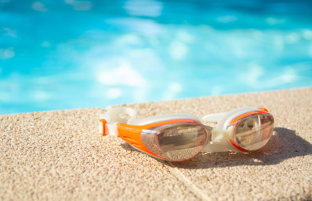 Swimming goggles lie at the edge of the blue pool on a sunny dayの写真素材