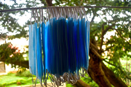 A bunch of blue colored face masks are being hanged on a cloth rod for drying purpose after cleaning...
