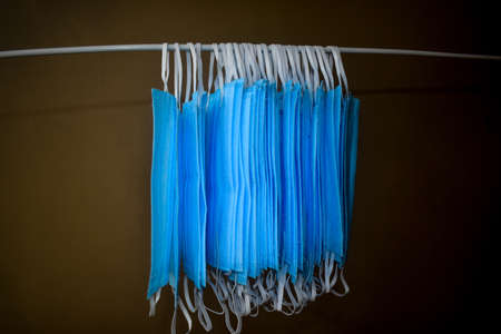A bunch of blue colored face masks are being hanged on a cloth rod for drying purpose after cleaning them for reuse. Reusable masks with clips hanged on a wireの写真素材