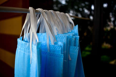 A bunch of blue colored face masks are being hanged on a cloth rod for drying purpose after cleaning them for reuse. Reusable masks with clips hanged on a wireの写真素材