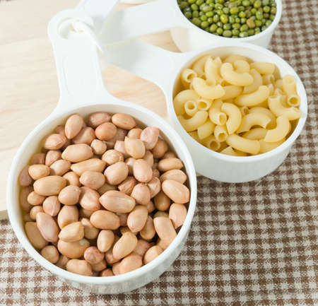 Carbohydrate Foods, Raw Pasta, Rice, Peanuts and Mung Beans in Plastic Measuring Cups.の写真素材