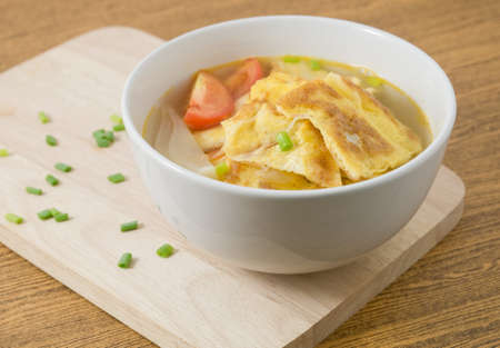 Thai Cuisine and Food, Thai Omelet Soup with Tomatoes, Onion and Chopped Scallion on Wooden Cutting Board.の写真素材
