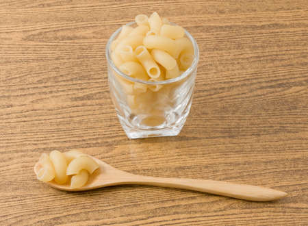 Food and Cuisine, Uncooked Elbow Macaroni or Gomiti Pasta in Glass Cup and Wooden Spoon.の写真素材