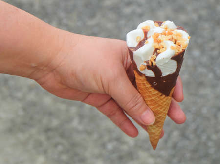 Hand Holding Vanilla Ice Cream with Chocolate and Nut in A Waffle Cone.