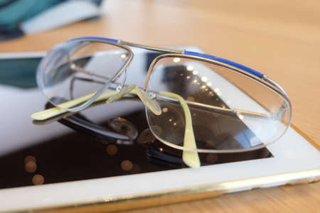Beautiful Reading Glasses with Tablet Computer on The Wooden Table in A Working Day.の写真素材