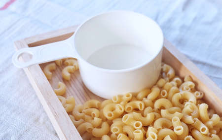 Food and Cuisine, Uncooked and Dried Elbow Macaroni Pasta in Wooden Tray with Plastic Measuring Cup.