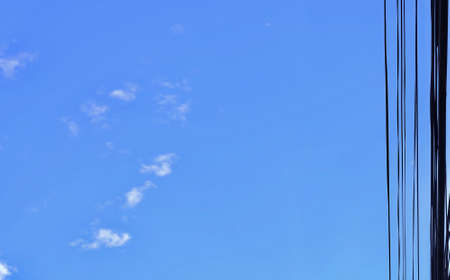 Chaos of Wires and Telephone Line Against on The Blue Sky with Fluffy White Clouds with Copy Space for Text Decorated.の写真素材