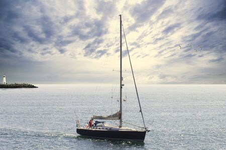 blue sailboat leaving the harborの写真素材
