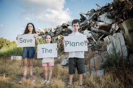 Save the planet. young kids holding signs standing in a huge junkyardの写真素材