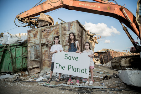 Save the planet. young kids holding signs standing in a huge junkyard