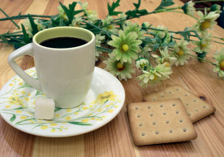 cup of coffee with piece of sugar on saucer and cookies on table against background of flowersの写真素材
