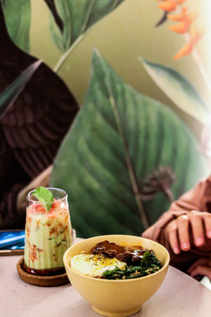 a glass of avocado juice with ice and boiled noodles filled with eggs and vegetables
