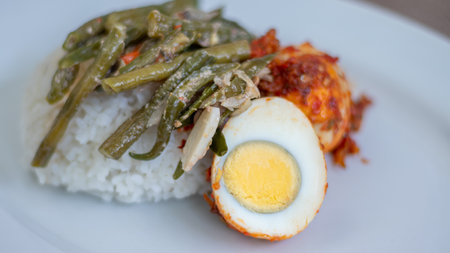 A plate of rice with egg balado and long bean sauce, chili sauce filled with eggs, anchovies and tofu. Served in a bowl on a gray background. Selected focus.の写真素材