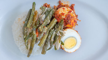 A plate of rice with egg balado and long bean sauce, chili sauce filled with eggs, anchovies and tofu. Served in a bowl on a gray background. Selected focus.の写真素材