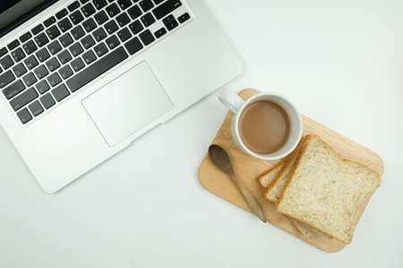 Sliced Whole wheat bread and a cup of coffee on Chopping Wood and laptop on a white backgroundの写真素材