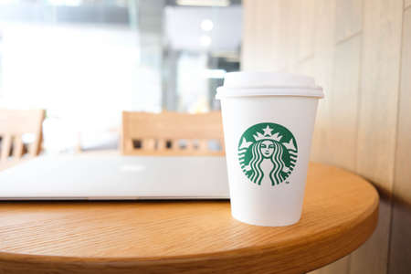 BANGKOK, THAILAND - JUN 15, 2018: White coffee cup with Starbucks logo and laptop on wooden table.のeditorial素材