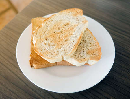 Two slices toast bread in the white plate on wooden table.の写真素材