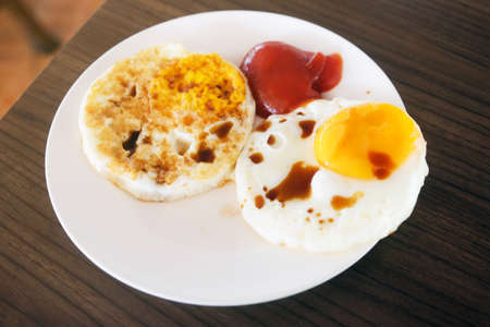 Two fried eggs with tomato sauce and soy sauce in white plate on wooden table for breakfast.の写真素材