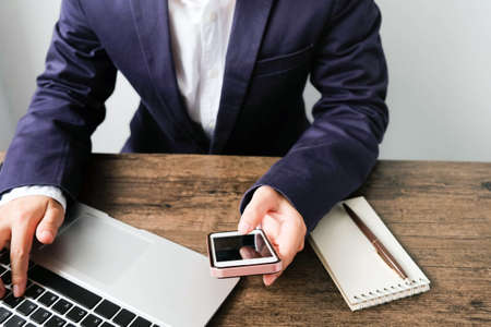 Hands of Business man typing keyboard laptop and holding smart phone on the wooden table.の写真素材