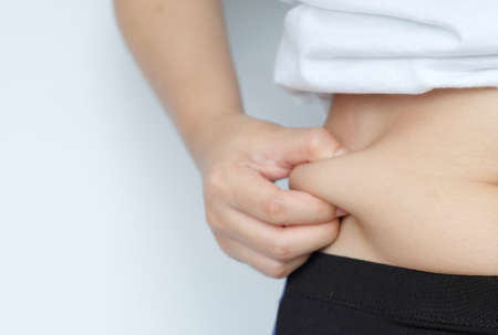 Side of woman hand catching fat body belly paunch , diabetic risk factorの写真素材