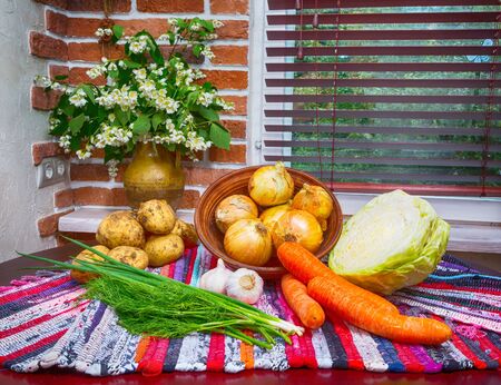 a fragment of the kitchen. vegetables potatoes, carrots, garlic, cabbage, green onionson a wooden table. tablecloth handmade photo in old style of the image.の写真素材