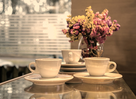 three cups of coffee in white mugs in the interior against the window, a vase of flowers vintage style photography effects. still lifeの写真素材