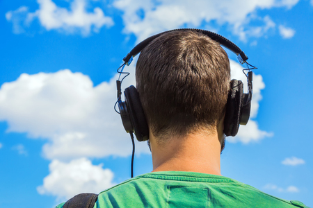 Man in headphones listening to the world against a blue sky with clouds