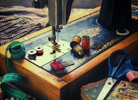 Old sewing machine and accessories for sewing, scissors, needles and tailor tape on the table. The concept of sewing accessories. Retro toningの写真素材